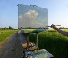 a person is painting on an easel in a field with green grass and blue sky