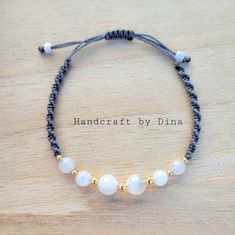 a bracelet with white beads and gold accents on a wooden surface, that says handcraft by dinaa