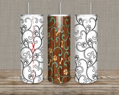 three tumbles with designs on them sitting on top of a wooden table in front of a wall