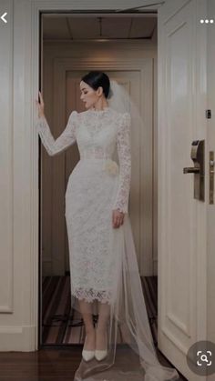 a woman in a white wedding dress is standing at the door with her veil over her head