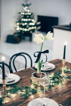 a dining room table set for christmas with candles, plates and flowers in the center