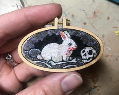 a hand holding a small embroidered badge with a white rabbit and skull on it's side