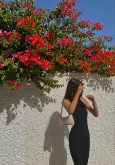 a woman standing in front of a white wall with red flowers on the planter