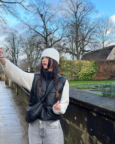 a woman holding an umbrella while standing next to a brick wall with trees in the background