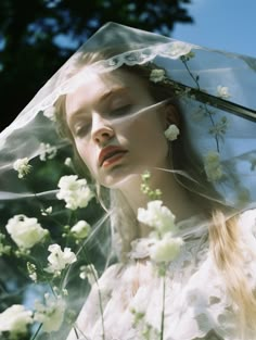 a woman wearing a veil with flowers on her head and in the background is a tree