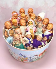 a bowl filled with lots of small dolls sitting on top of a pink tablecloth