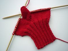 a red knitted object with two knitting needles