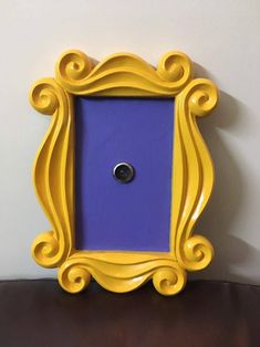 a purple and yellow frame with a black button on the bottom is sitting on a brown table