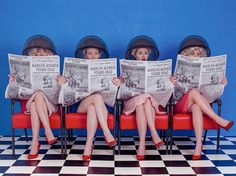 three women sitting on a red bench with hats over their heads and reading the paper