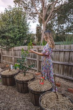 a woman in a dress standing next to several pots filled with plants and dirt on the ground