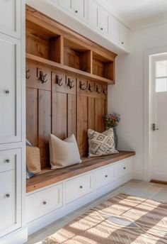 a wooden bench sitting under a window next to a white wall with hooks on it