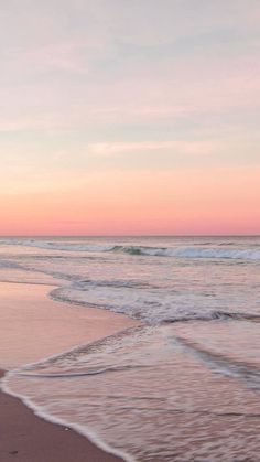 an ocean beach with waves coming in to shore and the sun setting on the horizon