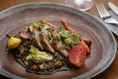 a plate with meat, rice and vegetables on it sitting on a table next to silverware