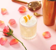 an orange slice on top of a drink next to rose petals and gold shakers