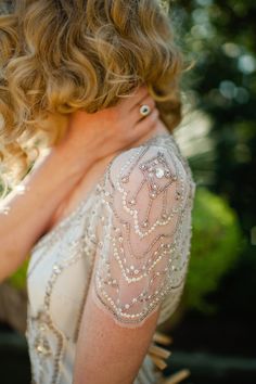 a woman with curly hair wearing a white dress and holding her hand on her shoulder