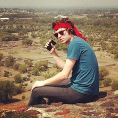 a man sitting on top of a rock next to a red bandanna holding a cell phone