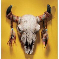 an animal's skull is adorned with feathers and beads on a yellow wall background