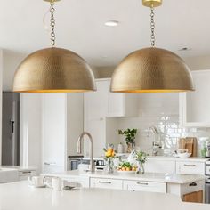 two pendant lights hanging from the ceiling in a kitchen with white cabinets and countertops