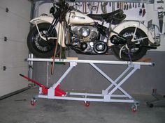 a motorcycle is on top of a work stand with tools hanging from the wall behind it