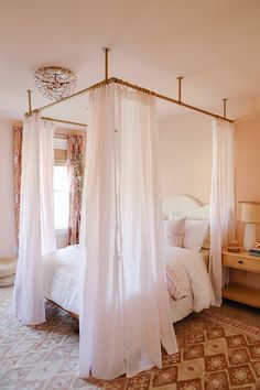 a white canopy bed sitting inside of a bedroom next to a dresser and lamp on top of a rug