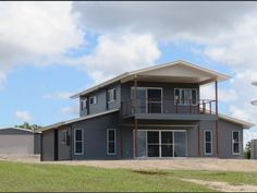 a large gray house sitting on top of a lush green field under a cloudy blue sky