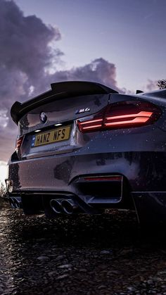 the back end of a silver bmw car parked on top of a rocky beach at sunset