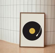 a black and yellow record on a white tiled wall next to a brown framed print