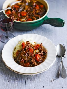 a white plate topped with meat and mashed potatoes next to a bowl of stew