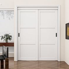 an empty room with two white doors and a black chair in the corner, next to a wooden table