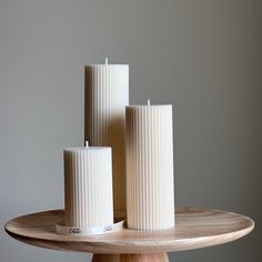 three white candles sitting on top of a wooden table