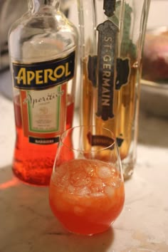 an orange drink in a glass next to two bottles