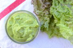 some lettuce is next to a small bowl of green sauce on a napkin