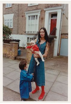 a woman holding two children in front of a house