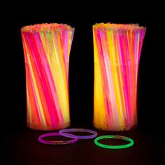 two large vases with neon colored sticks in the center and rings around them on a black background