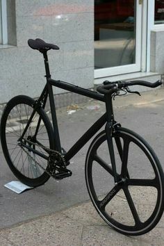 a black bike parked on the side of a street next to a building with windows