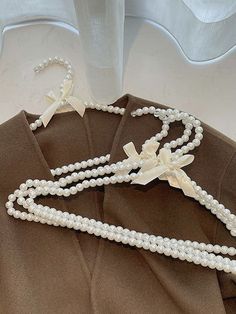 two necklaces with pearls and bows on top of a brown shirt, next to a white vase