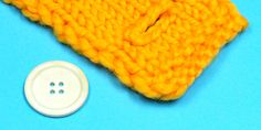 a yellow knitted object next to a white button on a blue surface with a light colored background