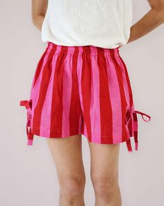 a woman wearing pink and red striped shorts with her hands on her hips, standing in front of a white wall