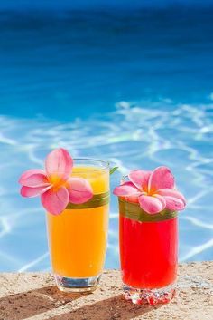 two glasses filled with different colored drinks next to a swimming pool and blue sky in the background