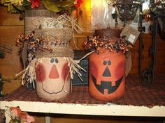 two decorated jars sitting on top of a shelf next to flowers and pumpkins with faces painted on them