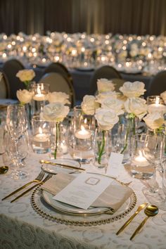 the table is set with silverware and white flowers in vases, candles and napkins