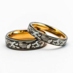 two gold and silver wedding rings with black floral designs on each band, set against a white background