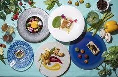 four plates with different foods on them sitting on a blue table cloth covered in leaves and flowers