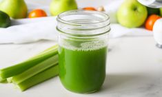 a glass jar filled with green liquid next to celery stalks and oranges