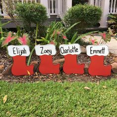 three wooden christmas stockings with name tags on them sitting in front of some bushes and flowers