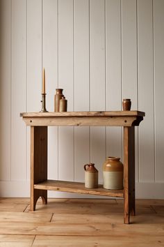 an old wooden table with candles and jars on it in front of a white wall