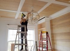 a person on a ladder working on a light fixture in a room with wood paneling