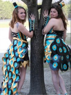 two women dressed in costumes standing next to a tree with their hands on the trunk