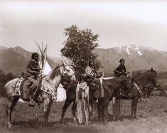 an old black and white photo of native americans on horses with mountains in the background