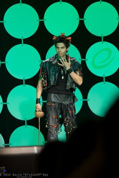 a man standing on top of a stage next to a green wall and holding a microphone